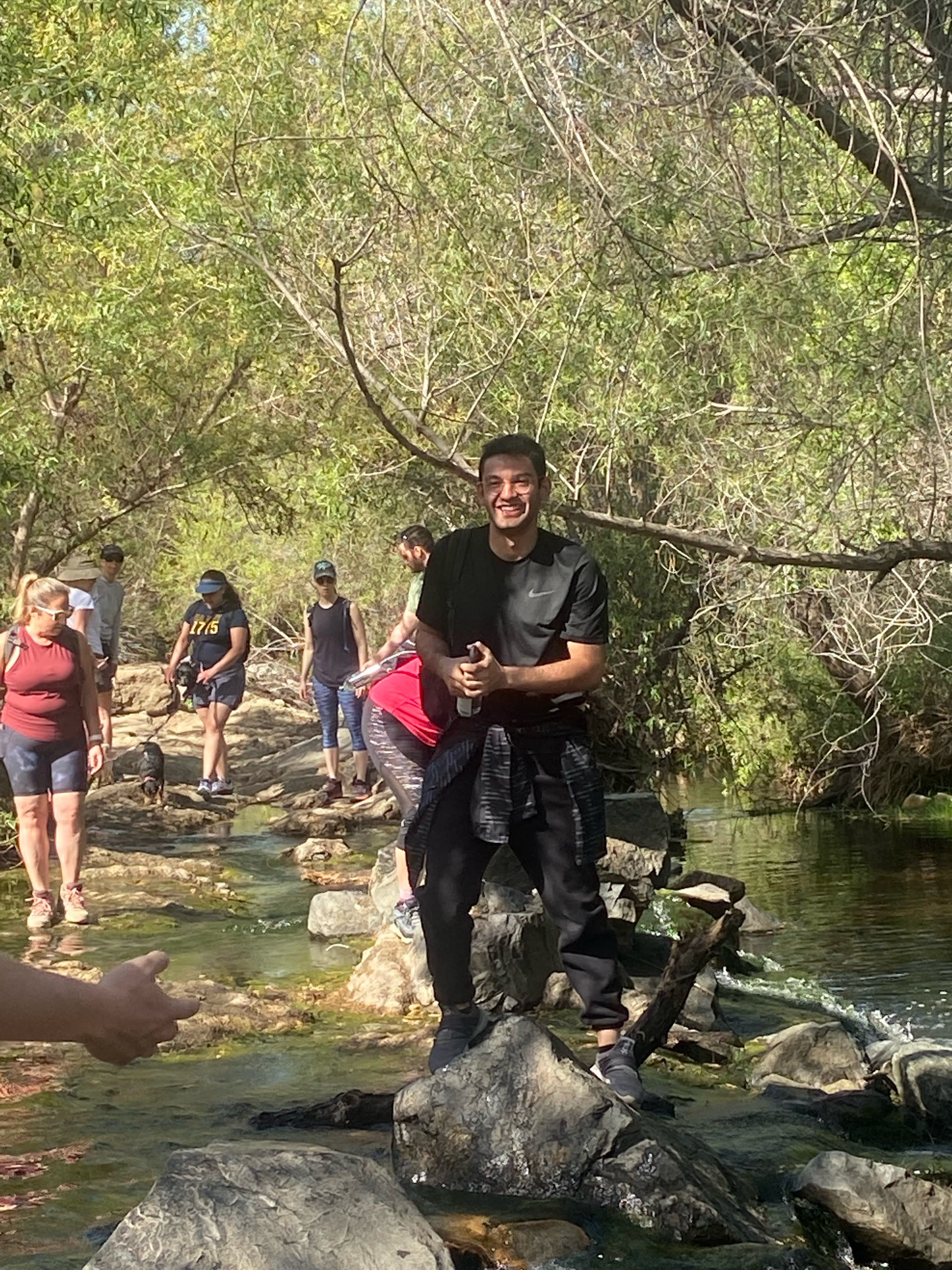 Qudsi grinning, standing on a rock in a creek on a hike