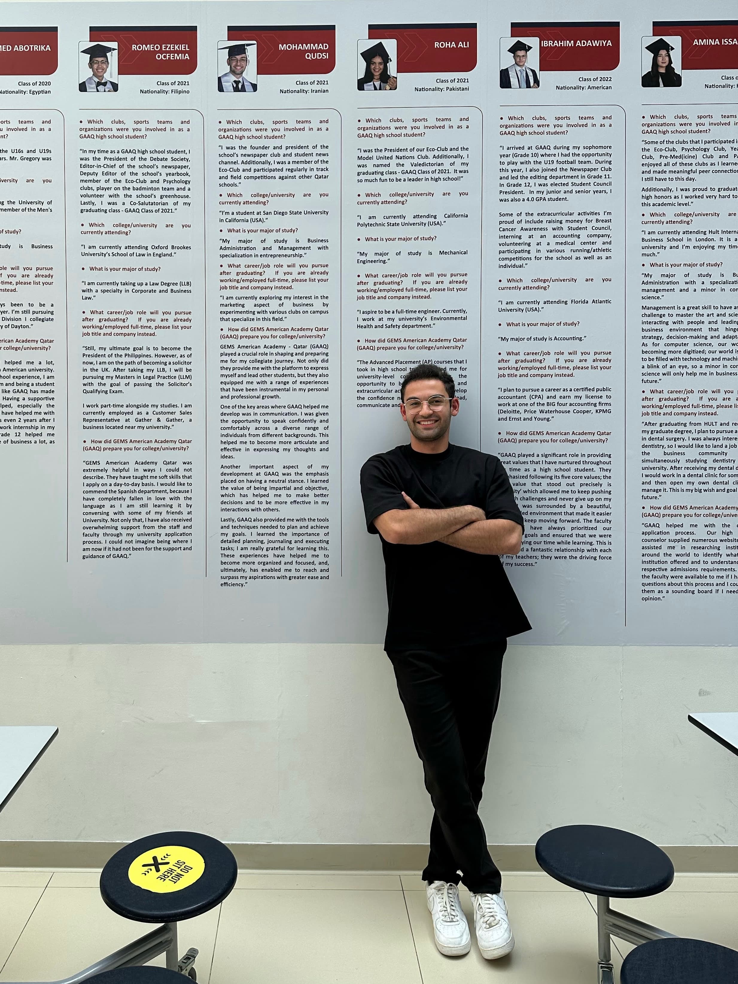 Qudsi standing beside his featured student spotlight on the school wall